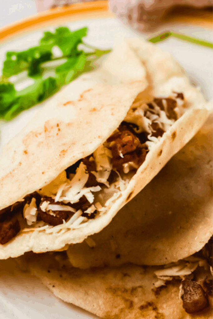 Close-up of authentic tacos al vapor filled with carne asada and melted cheese on a plate with fresh cilantro garnish.