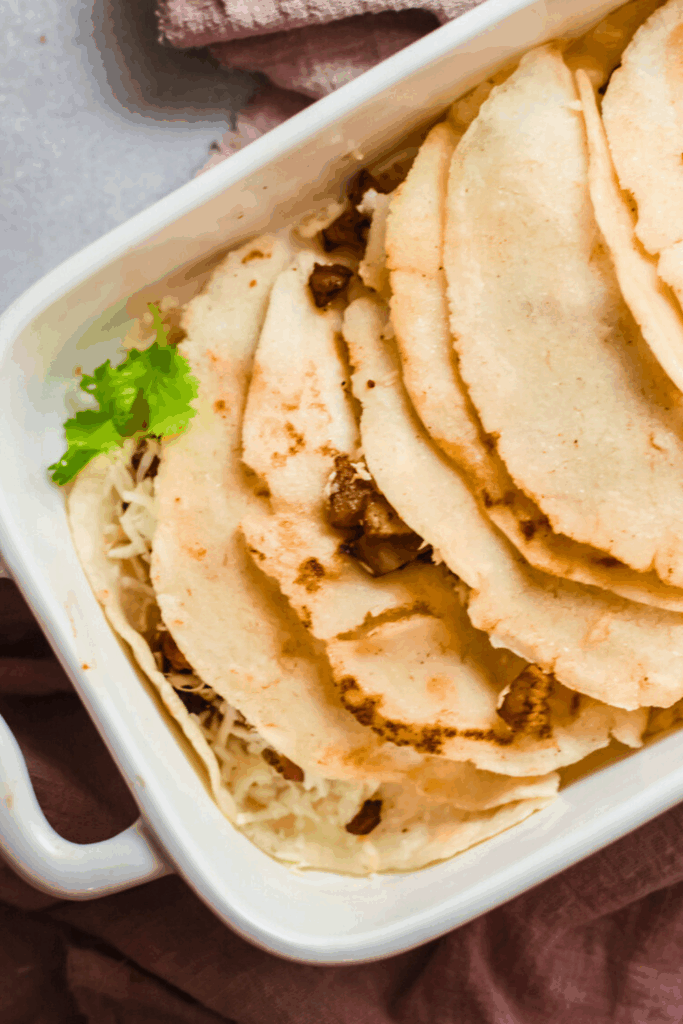 Stack of authentic tacos al vapor filled with carne asada and cheese in a white dish, garnished with fresh cilantro.