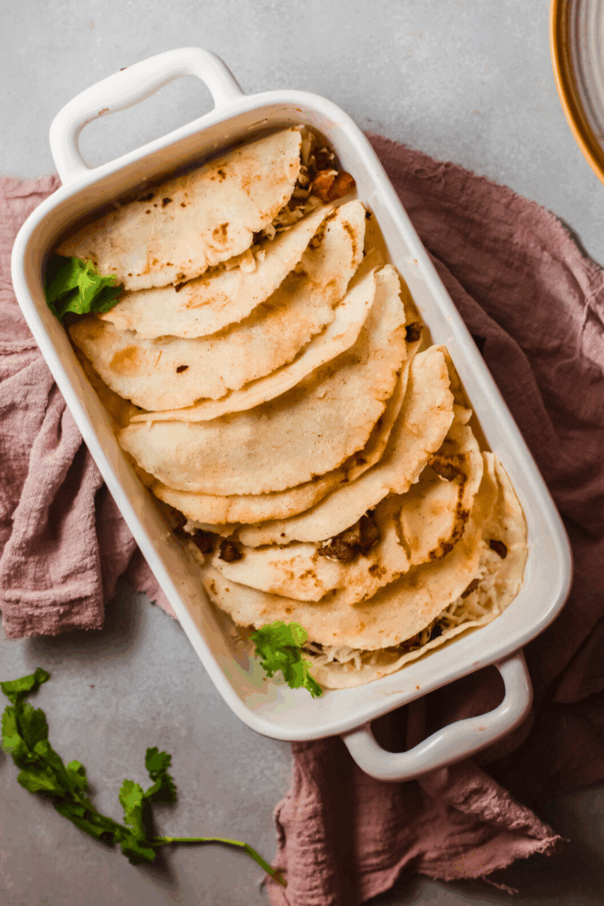 Homemade tacos al vapor arranged in a white baking dish, filled with carne asada and cheese, topped with fresh cilantro.