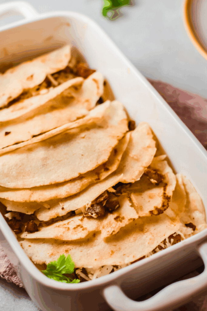 Mexican steamed tacos al vapor arranged in a white baking dish, filled with carne asada and cheese, and garnished with fresh cilantro.