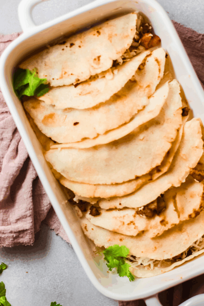 Authentic tacos al vapor arranged in a white baking dish, filled with carne asada and cheese, and garnished with fresh cilantro.