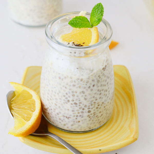 A serving of orange chia pudding in a glass jar on a yellow plate, styled with fresh orange slices and a spoon for a bright, healthy presentation.
