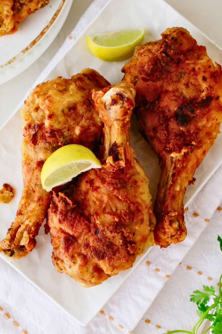 Golden brown Puerto Rican fried chicken drumsticks and thighs, crispy on the outside and juicy inside, served with lime wedges for a flavorful pollo frito meal.