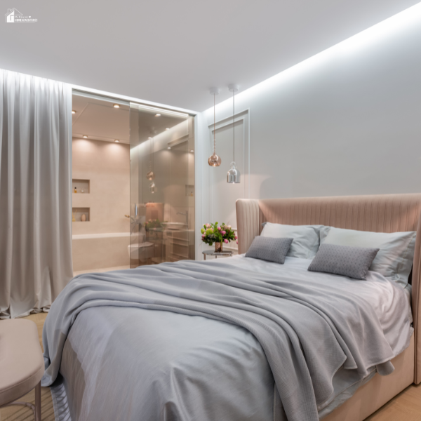 A cozy modern bedroom featuring a neatly made bed with soft linens, warm lighting, and a view into a stylish bathroom.