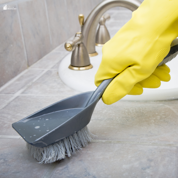 A gloved hand scrubs a tiled bathroom counter near a faucet with a bristle brush.