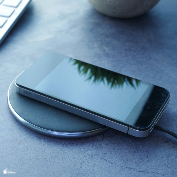 A smartphone resting on a wireless charging pad placed on a sleek gray desk near a keyboard.