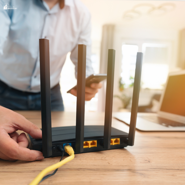 A person adjusts the cables on a wireless internet router placed on a wooden desk.
