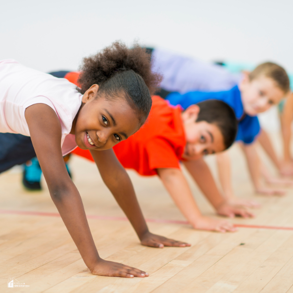 Children in active poses hold plank positions in a homeschool gym while smiling and looking ahead with enthusiasm.