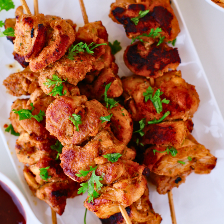 Grilled Puerto Rican pinchos served on skewers, garnished with fresh herbs, paired with bread and BBQ sauce, showcasing an easy pinchos recipe.