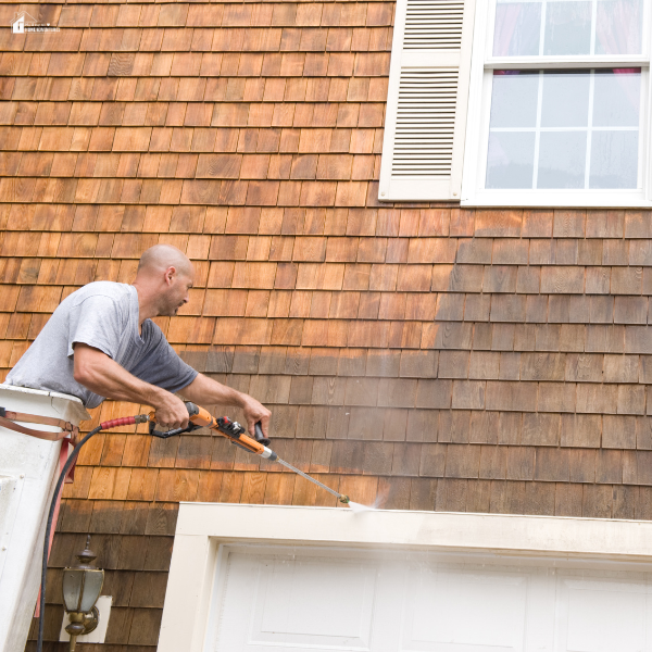 A man using a high power hose for cleaning the exterior walls of a home.