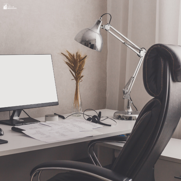 Modern home office setup with a computer monitor, headset, papers, and a silver desk lamp on a white desk.