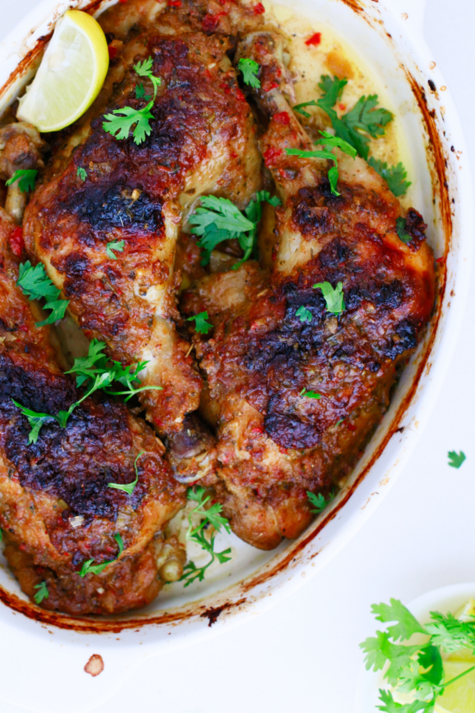 Top view of Puerto Rican baked chicken with crispy golden skin and fresh cilantro, served in a white baking dish with lime wedges for a traditional Caribbean dinner.