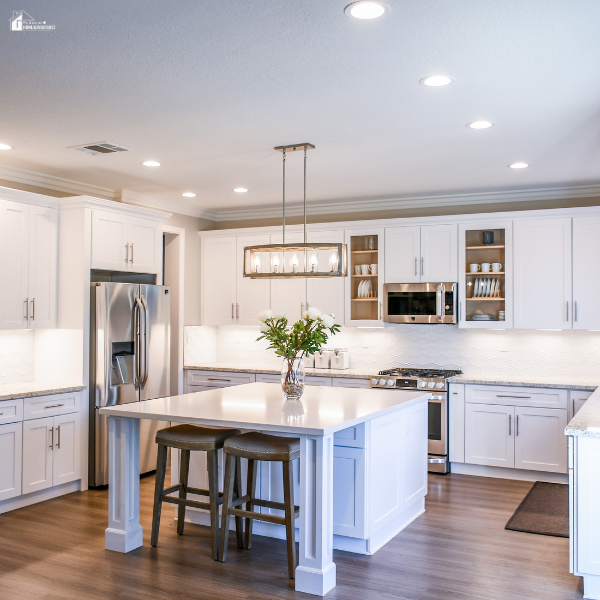A bright white kitchen with shaker cabinets, stainless steel appliances, and a center island with two wooden stools.
