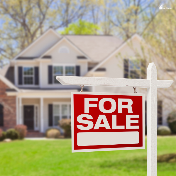 A large suburban house with a bright red for-sale sign displayed on the front lawn during springtime.