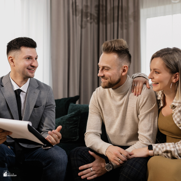 A couple sitting on a couch while discussing real estate plans with a professional agent in a modern living room.