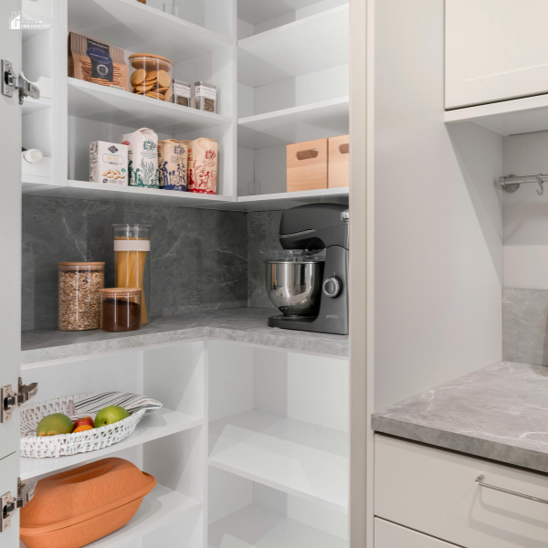 A neatly organized pantry with white shelving, labeled containers, and a stand mixer on a gray countertop.
