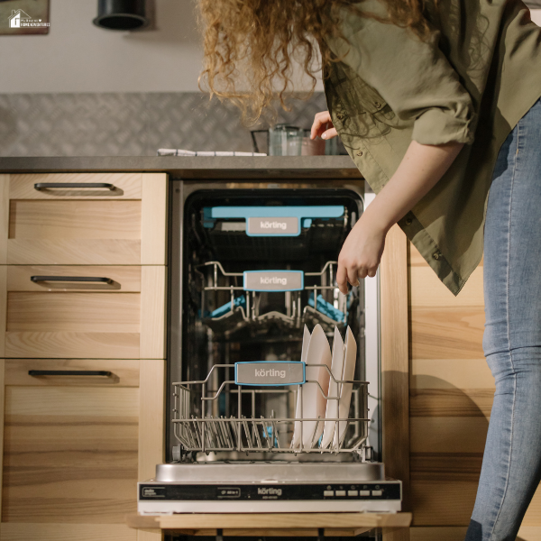 A woman loading white plates into the bottom rack of a dishwasher in a modern kitchen.