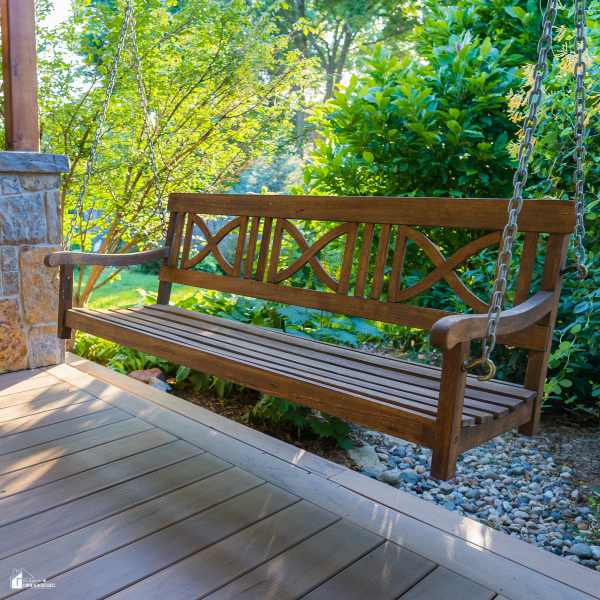 A wooden porch swing hanging from chains, surrounded by green shrubs and trees in a cozy backyard corner.