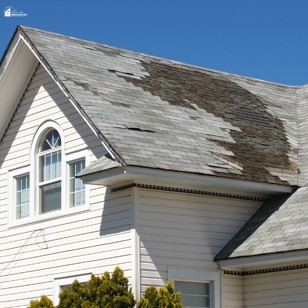 A house with a heavily weathered and damaged roof showing missing and curled shingles, needing a repair.