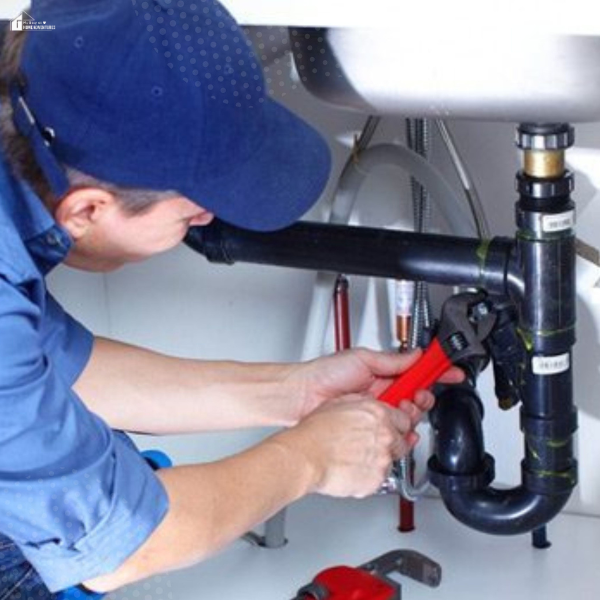 A plumber using a wrench to tighten black PVC pipes under a kitchen sink.