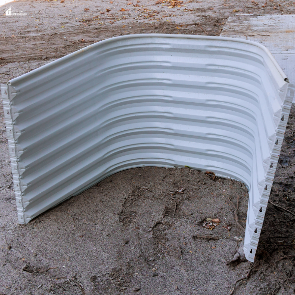 A single clean, white metal window well is placed on the ground, ready for installation next to a building.