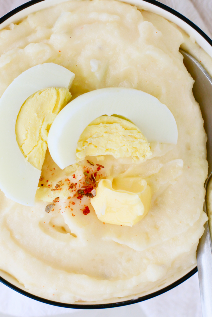 Close-up of Puerto Rican mashed potatoes with eggs, topped with sliced hard-boiled egg, butter, and adobo seasoning—an easy and creamy Caribbean side dish perfect for holiday meals or comfort food cravings.