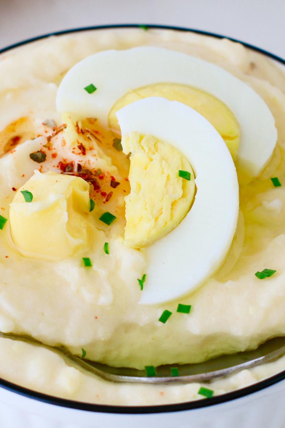 A bowl of creamy Puerto Rican mashed potatoes with eggs, topped with sliced hard-boiled egg, butter, and herbs—an authentic Caribbean side dish perfect for holiday meals and comfort food lovers.