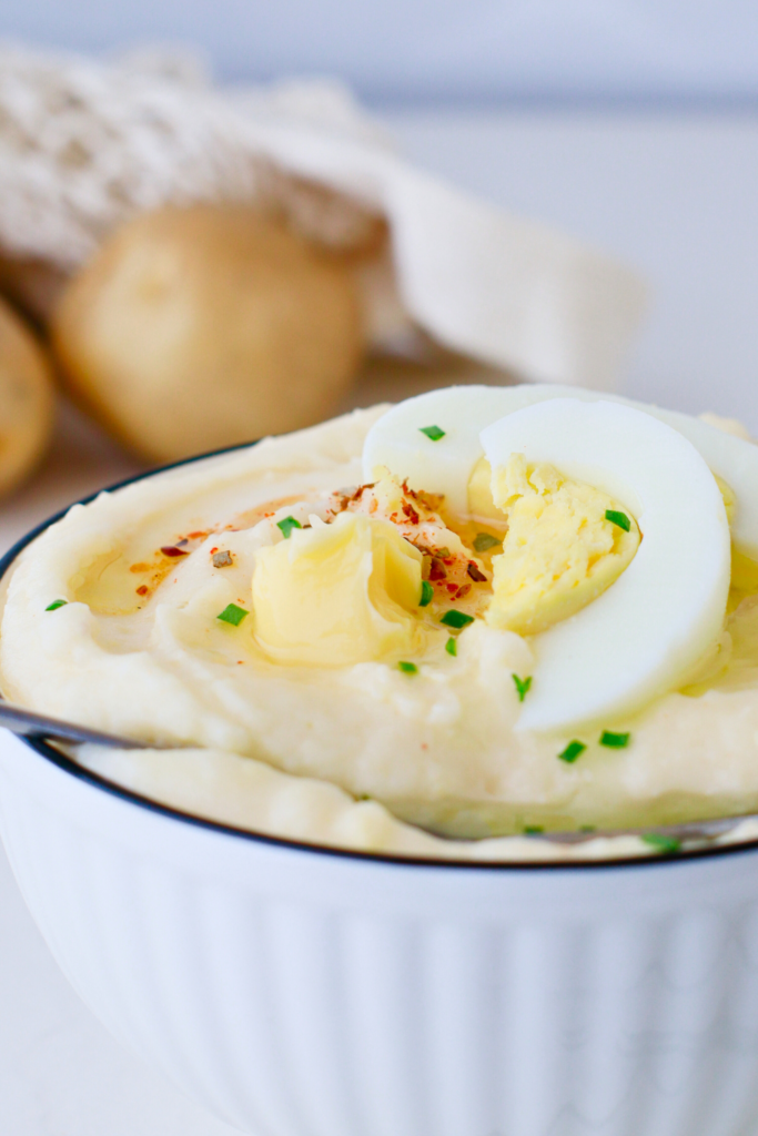 Creamy Puerto Rican mashed potatoes with eggs served in a white bowl, topped with butter, sliced hard-boiled egg, and herbs—an easy and flavorful Latin mashed potato recipe perfect for family meals or holiday gatherings.