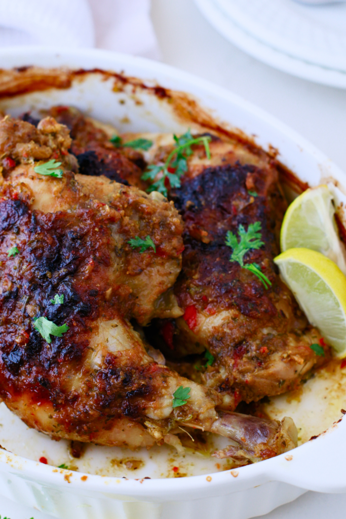 Golden and crispy Puerto Rican baked chicken (pollo al horno) fresh out of the oven, garnished with herbs and served with lime wedges in a white baking dish.