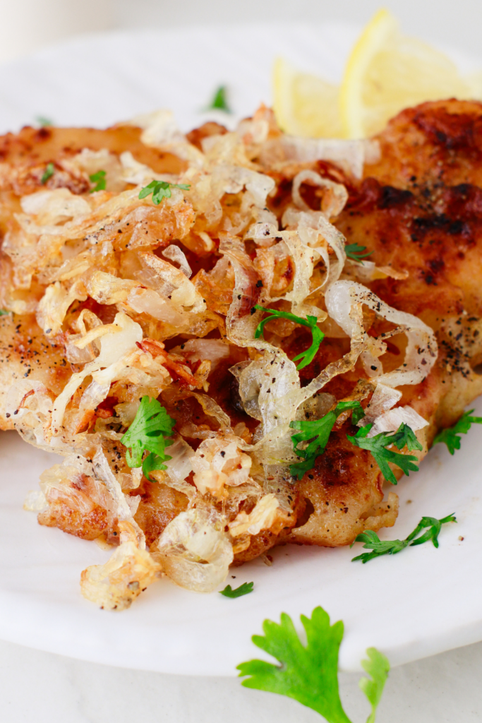 Crispy golden onions layered over juicy Cuban lemon chicken, garnished with herbs and coarse pepper.