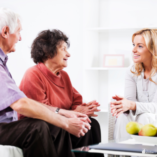 Two older adults and a younger woman sit together indoors, engaged in a calm and supportive conversation.