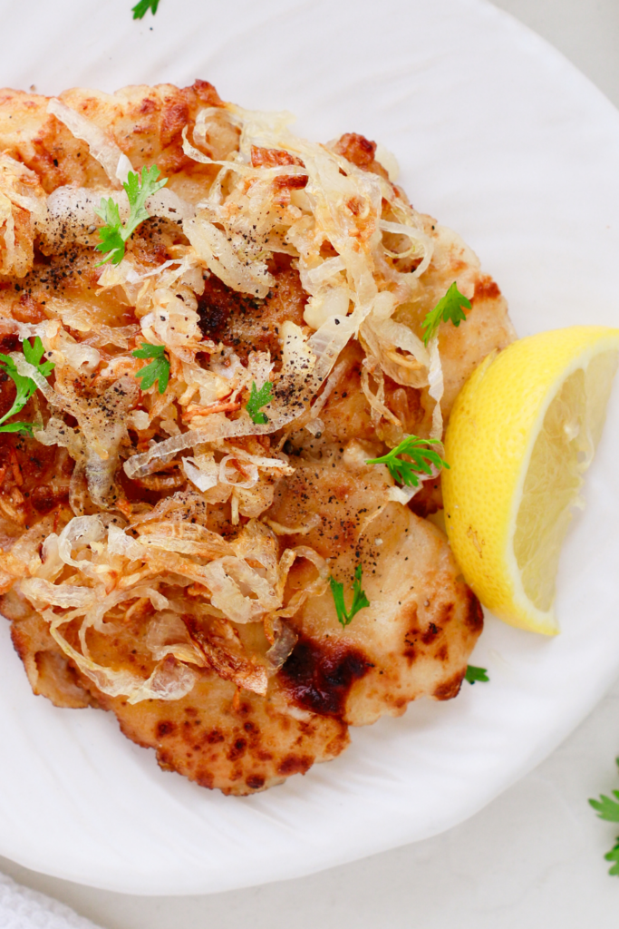 Top-down view of a full plate of Cuban lemon chicken with a lemon wedge and scattered parsley leaves.