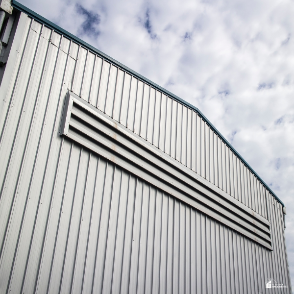 The upper portion of a large metal structure with horizontal ventilation slats under a cloudy sky.