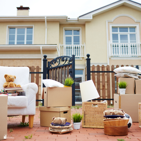 Boxes, plants, and household items sit outside a house, ready for relocating.