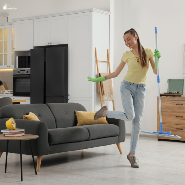 Smiling woman in gloves holds a mop while enjoying spring cleaning in a tidy modern living room.