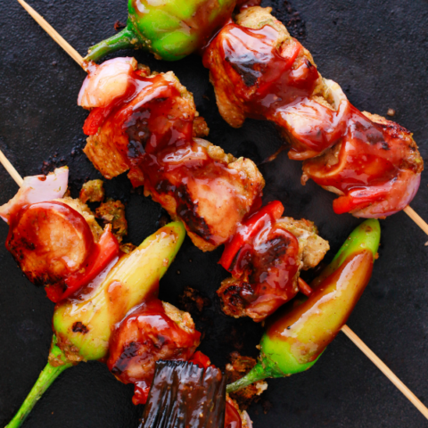 Puerto Rican Pinchos de Carne being brushed with barbecue sauce while grilling on a hot cast iron surface.