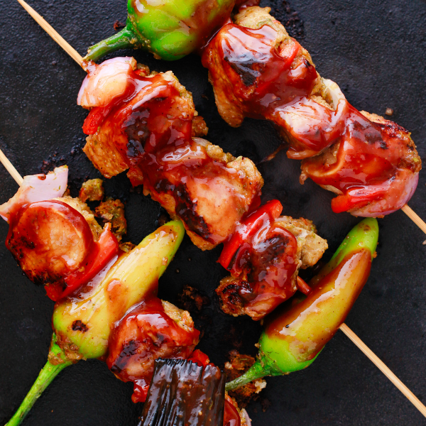 Puerto Rican Pinchos de Carne being brushed with barbecue sauce while grilling on a hot cast iron surface.