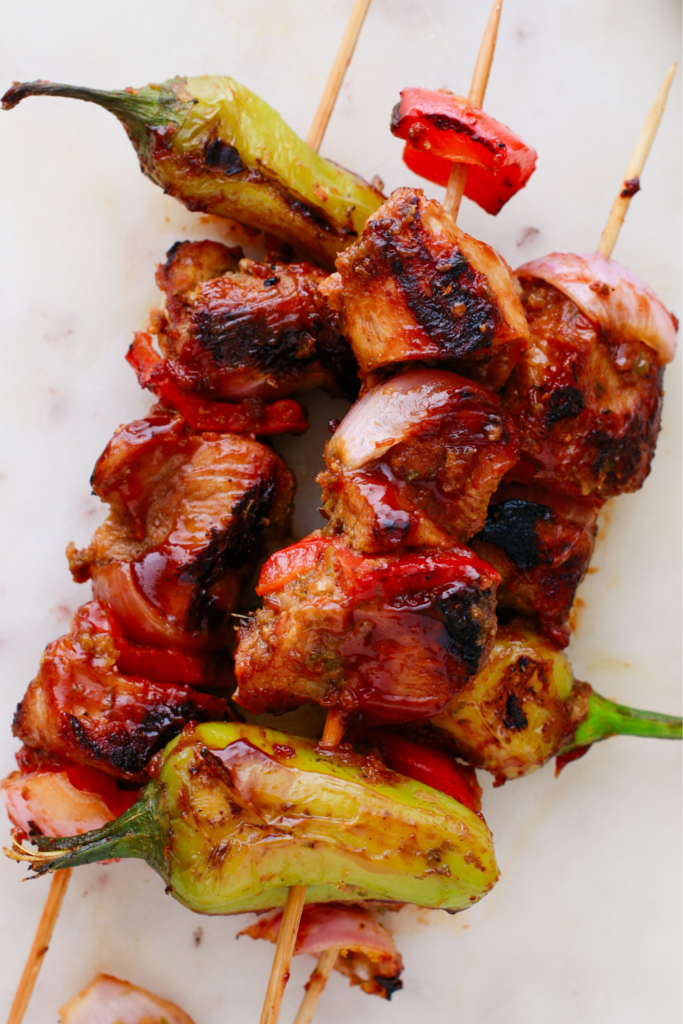 Puerto Rican Pinchos de Carne with grilled steak, shishito peppers, red bell peppers, and onions on wooden skewers.