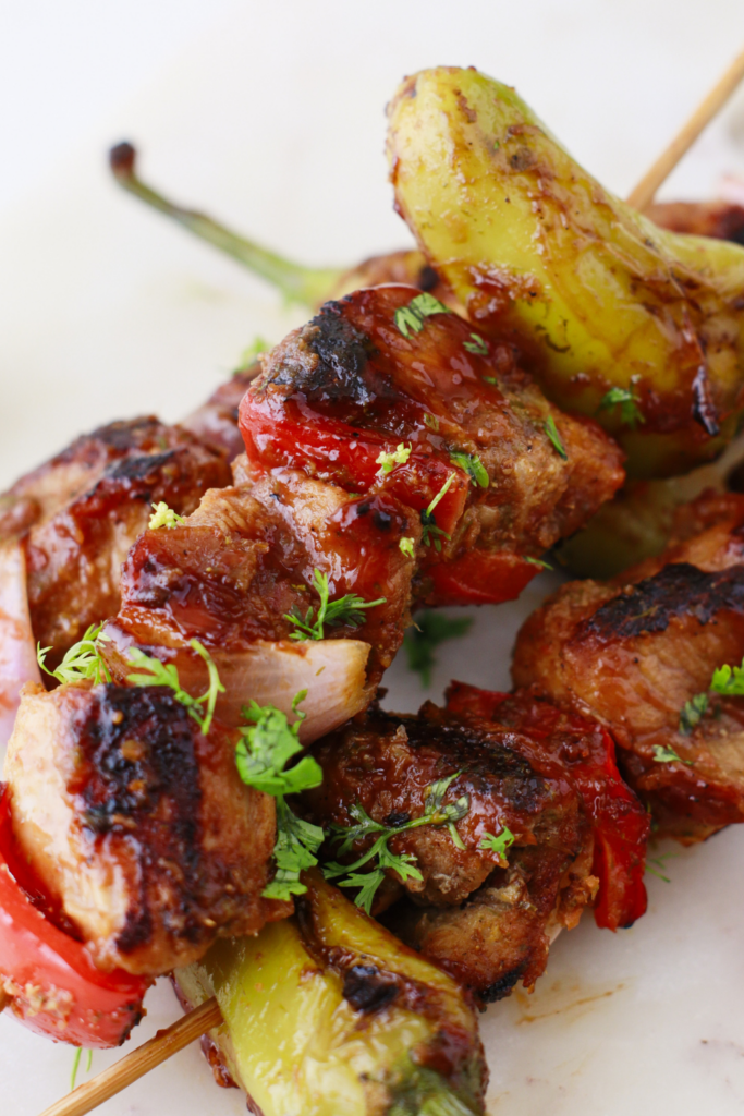 Close-up of Puerto Rican Pinchos de Carne showing juicy grilled steak skewers topped with fresh cilantro and colorful veggies.