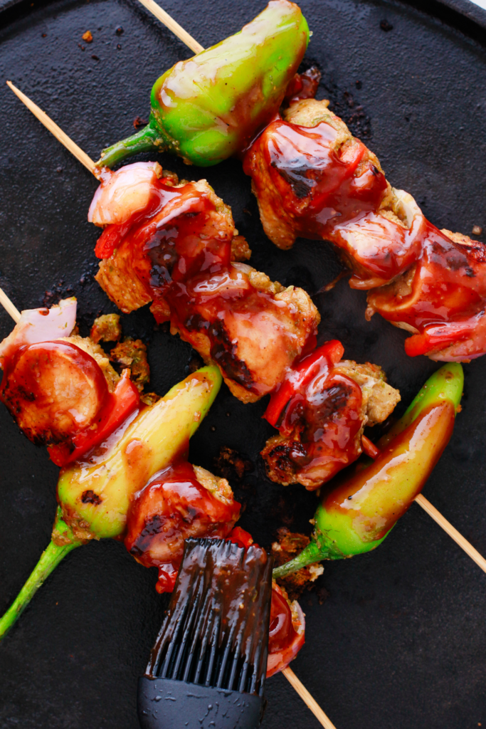 Puerto Rican Pinchos de Carne being brushed with barbecue sauce while grilling on a hot cast iron surface.