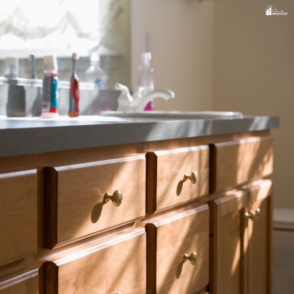 A bathroom vanity with natural wood cabinets and drawers under a sink with personal care items on the counter.