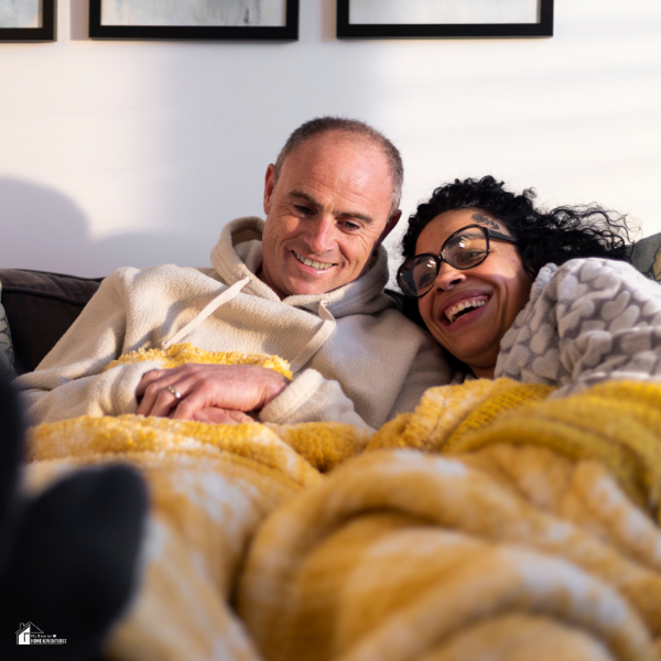A couple relaxes on the couch wrapped in cozy yellow blankets to stay warm indoors during winter.