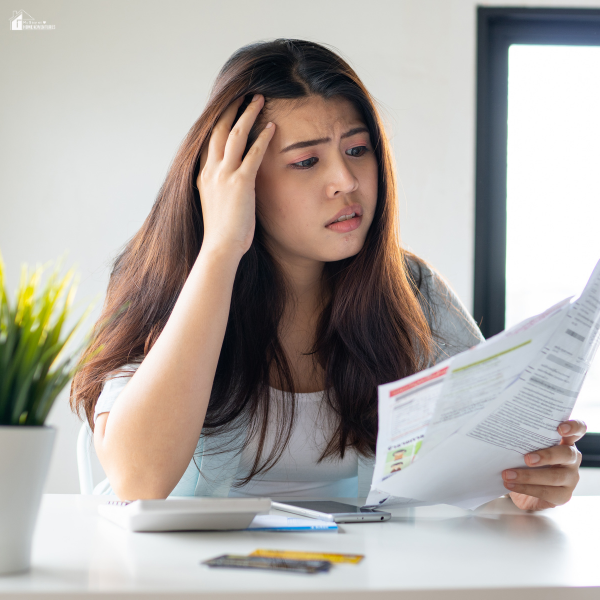 A concerned woman sits at a desk reviewing bills with a calculator and credit card in front of her.