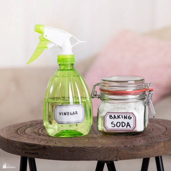Green spray bottle of vinegar and glass jar of baking soda used for simple, low-effort shower deep-cleaning.