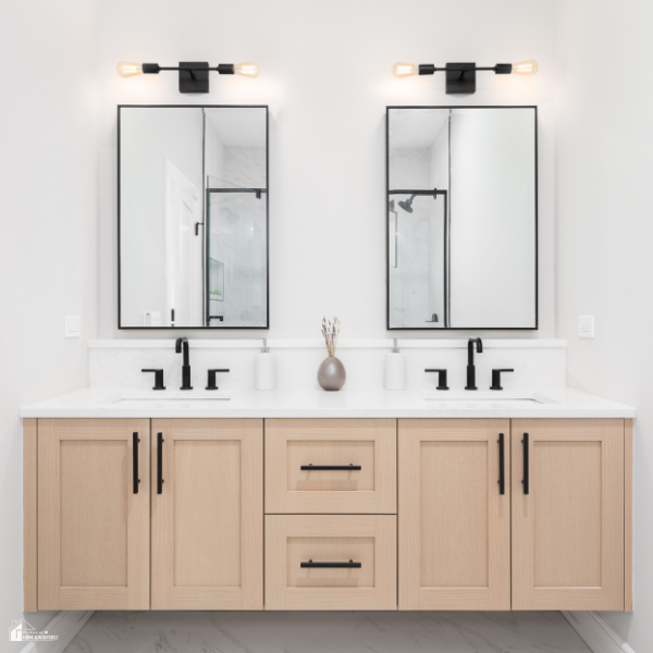 A modern bathroom vanity with light wood cabinets, black hardware, and two mirrors above double sinks.