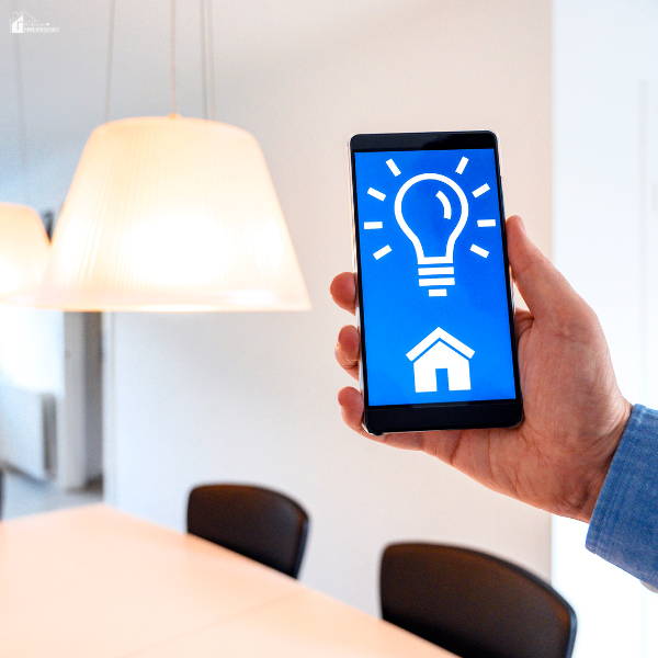 A person holds a smartphone showing a smart home energy control app in a well-lit dining area.