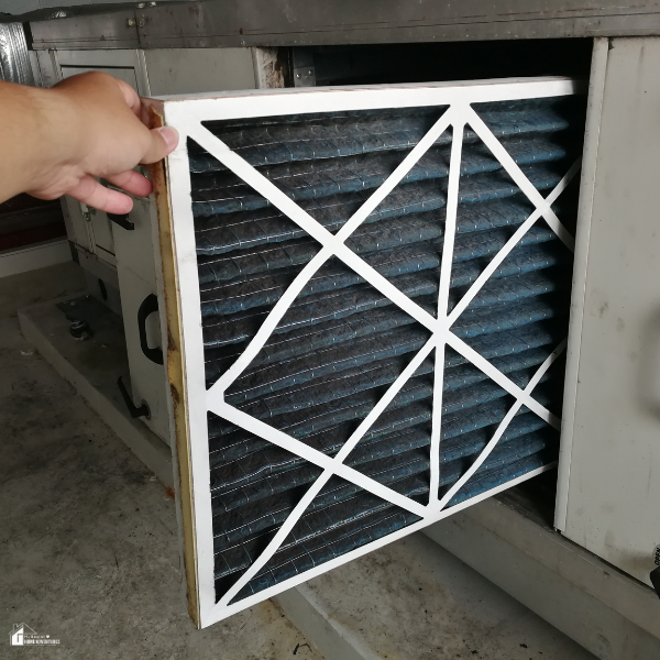 A person replaces a dirty air filter in a heating system to improve efficiency and lower energy use.