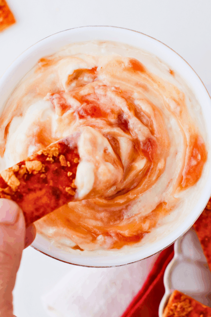 Close-up of Puerto Rican guava dip in a white bowl, showing its creamy swirl texture with a cracker dipped in, a sweet and savory tropical appetizer for parties.
