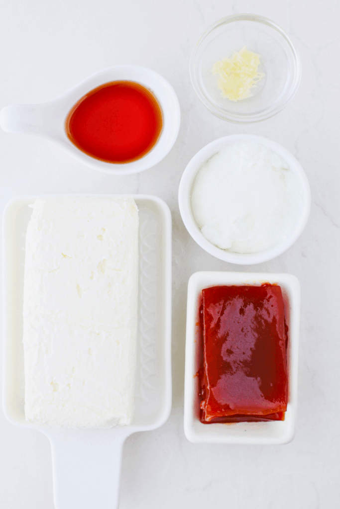 Ingredients laid out on a white surface to make Puerto Rican guava dip, including guava paste, cream cheese, sour cream, garlic, and honey for a creamy Caribbean appetizer.