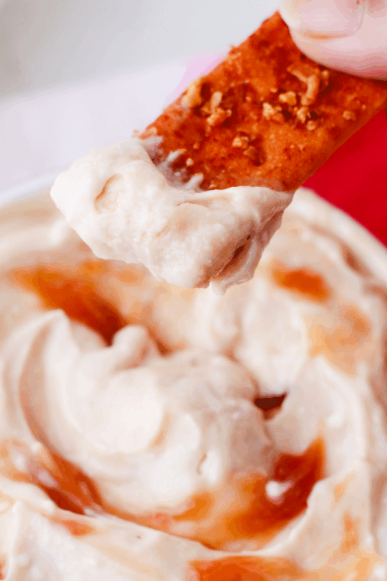 Close-up of a cracker dipped into creamy Puerto Rican guava dip, a sweet and savory tropical appetizer with smooth texture and swirls of guava.